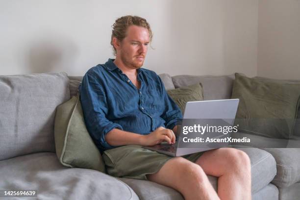 man works on laptop on sofa - navy blue living room stock pictures, royalty-free photos & images