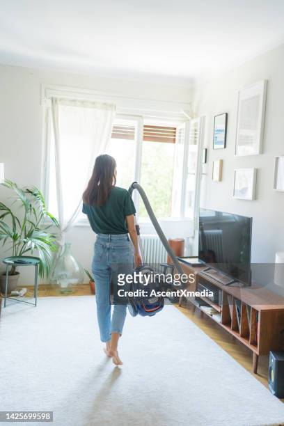 young woman vacuums living room carpet - navy blue living room stock pictures, royalty-free photos & images