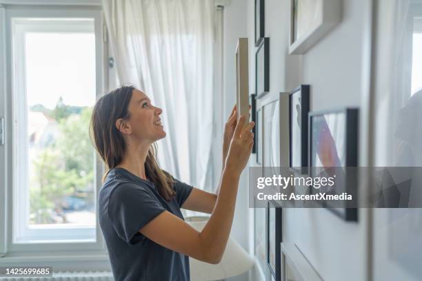 giovane donna mette l'immagine sul muro nel soggiorno - moving image foto e immagini stock