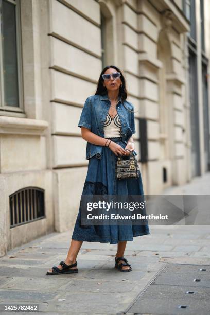 Gabriella Berdugo wears blue sunglasses, gold chain pendant necklaces, a beige with embroidered black pattern wool heart-neck / cropped top, a blue...