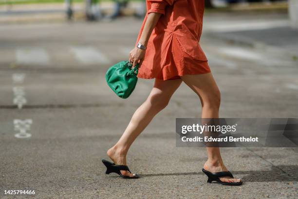 Julia Comil wears an orange cotton shirt, matching orange cotton shorts, a silver watch, rings, a green shiny leather puffy handbag from Hereu, a...