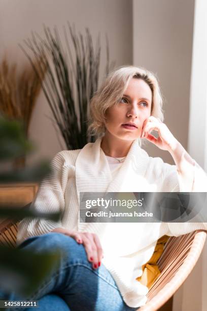 blonde woman sitting in living room at home with sad expression. - escena de tranquilidad fotografías e imágenes de stock