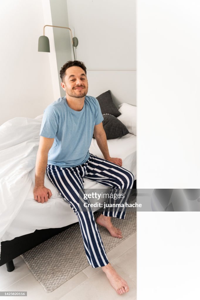 Relaxed man stretching sitting on the edge of the bed after waking up.