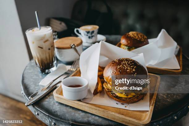 delicious cheeseburgers freshly served with fries on a wooden board on dining table, with coffee by the side in a restaurant. food and lifestyle concept - comfort food stock pictures, royalty-free photos & images