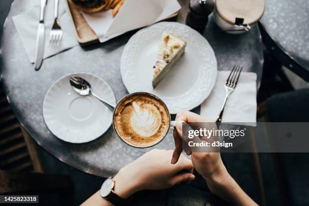 overhead view of a woman sitting at a table in cafe, drinking coffee and having a piece of cake. enjoying a relaxing moment. coffee break. food, people and lifestyle concept - coffee cake stockfoto's en -beelden