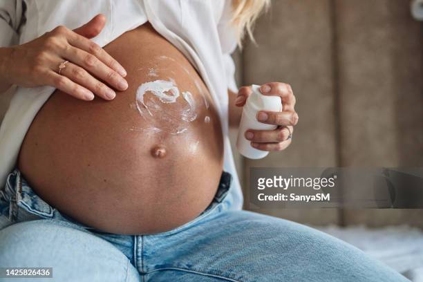 woman applying moisturizer on pregnant belly - stretch mark stock pictures, royalty-free photos & images