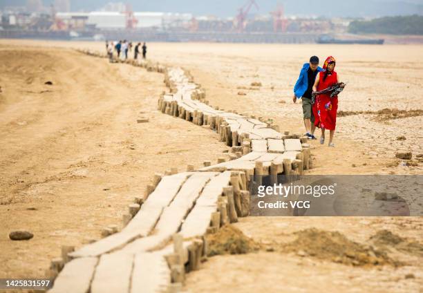 Tourists walk beside an ancient bridge which emerges from dried Poyang Lake on September 21, 2022 in Jiujiang, Jiangxi Province of China. The...