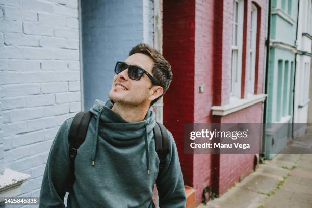 young man enjoying himself while getting to know the city, looking at the urban scenery. - discovery bags walking stock-fotos und bilder