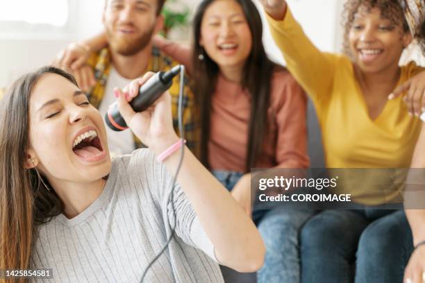 young woman passionately singing along with her friends at home. concept of well-being and friendship. - party friends home guitar singers fotografías e imágenes de stock