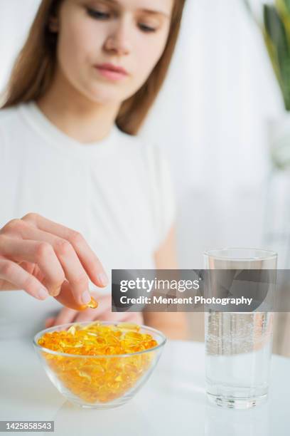 young female doctor nutritionist hand takes pills fish oil omega-3 supplements capsules from a bowl on the white glass table - fish oil stock photos et images de collection