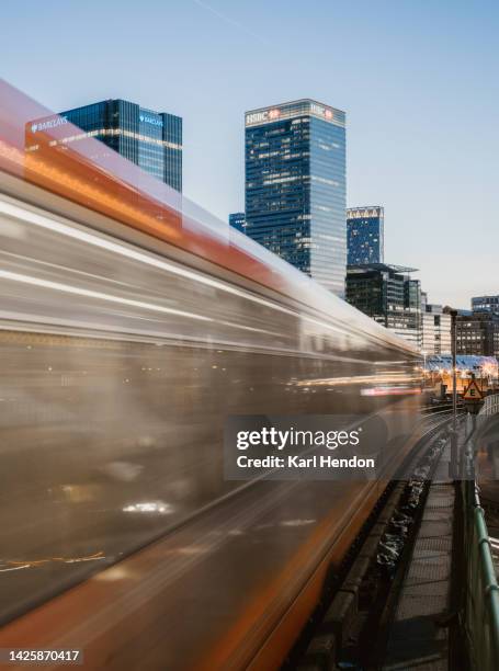 a long exposure view of a train passing the canary wharf skyline, london - dusk - modern traveling stock pictures, royalty-free photos & images