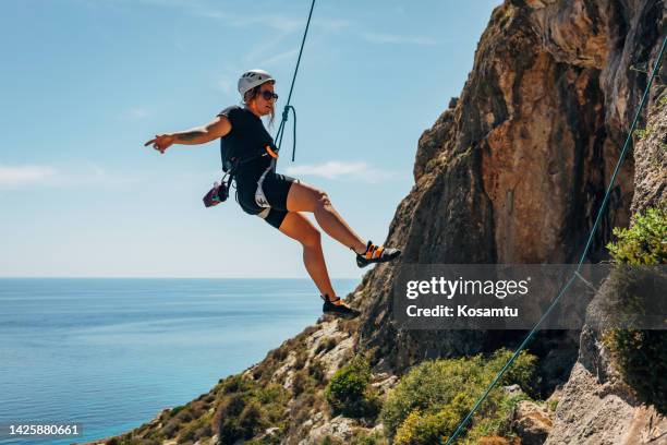 mujer milenaria bajando del acantilado después de escalar rocas. escaladora con casco haciendo rappel por un acantilado empinado - rápel fotografías e imágenes de stock