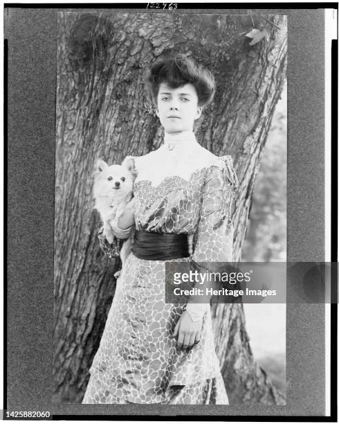 Alice Roosevelt Longworth, three-quarter length portrait, standing in front of tree, facing slightly left, holding small dog, circa 1902. [Daughter...