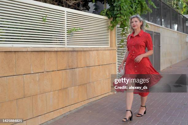 schönes junges mädchen in einem roten kleid geht die stadtstraße entlang - frau kleid stock-fotos und bilder