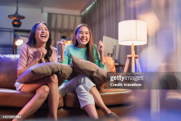 two asian young female women friend watching tv together in living room with happy victory success emotion while watching cheering football soccer match on tv at home cheering and very happy night program - glee tv program stockfoto's en -beelden