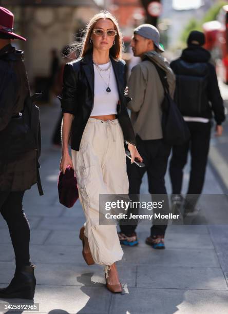 Guest is seen wearing beige sunglasses, black leather blazer, white cropped shirt, silver necklaces, oversize beige nylon parachute pants, purple...