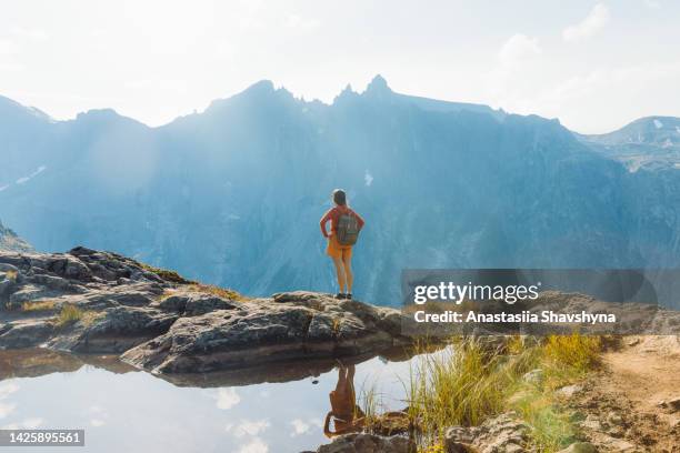 rear view of a female backpacker hiking in the mountains by the lake in norway during autumn day - blue shorts stock pictures, royalty-free photos & images