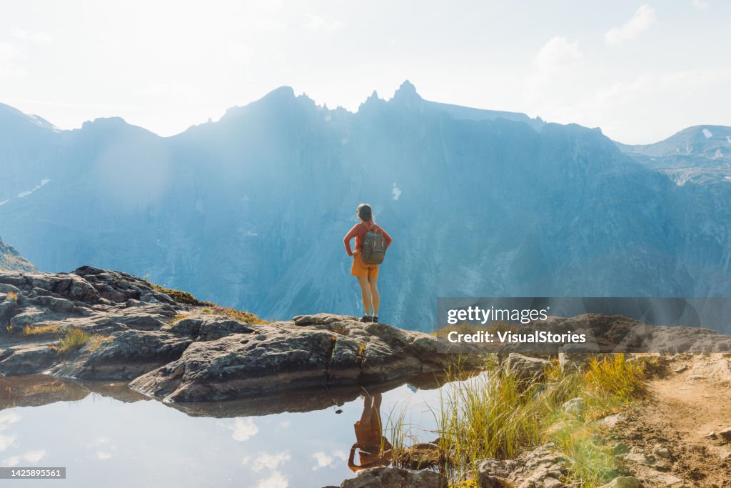 Rear view of a female backpacker hiking in the mountains by the lake in Norway during autumn day