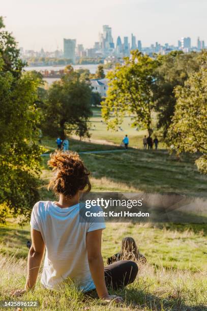 a woman sits in a london park looking at a sunset view of the city - london park stock pictures, royalty-free photos & images