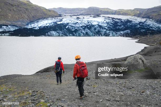 guixde und jugendliche wanderer in kletterausrüstung rückansicht wanderung in richtung sólheimajökull-gletscher - icepick stock-fotos und bilder