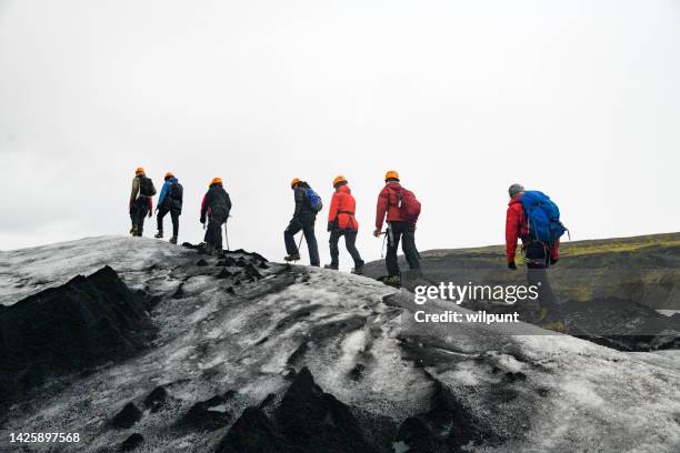 side view guided tour group of hikers with crampons navigating exploring sólheimajökull glacier - icepick stock pictures, royalty-free photos & images