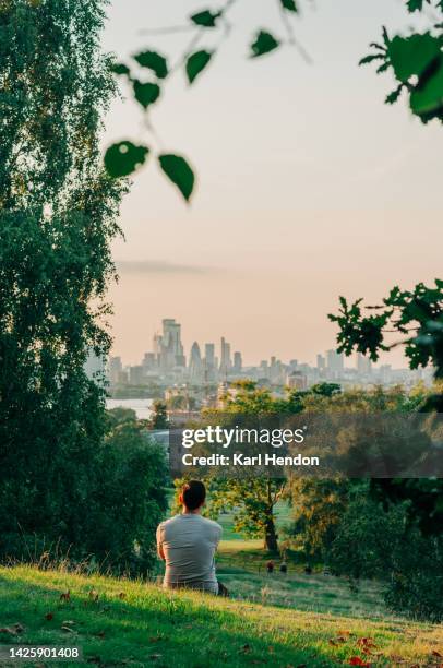 a man sits in a london park looking at a sunset view of the city - londres imagens e fotografias de stock