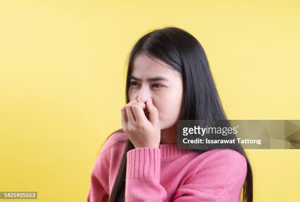 bright young woman covers his nose due to bad smell  isolated on yellow background - bad breath stockfoto's en -beelden