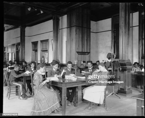 Interior view of library reading room with male and female students sitting at tables, reading, at the Tuskegee Institute, circa 1902. [African...