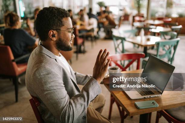 man is having online call at café while sitting and working - busy coffee shop stock pictures, royalty-free photos & images