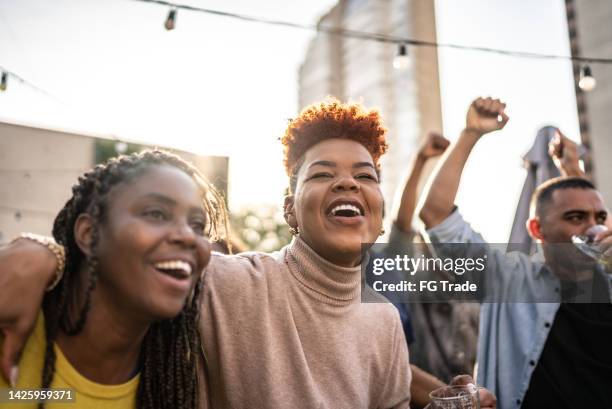sports fans watching a match and celebrating at a bar rooftop - black female dj stock pictures, royalty-free photos & images