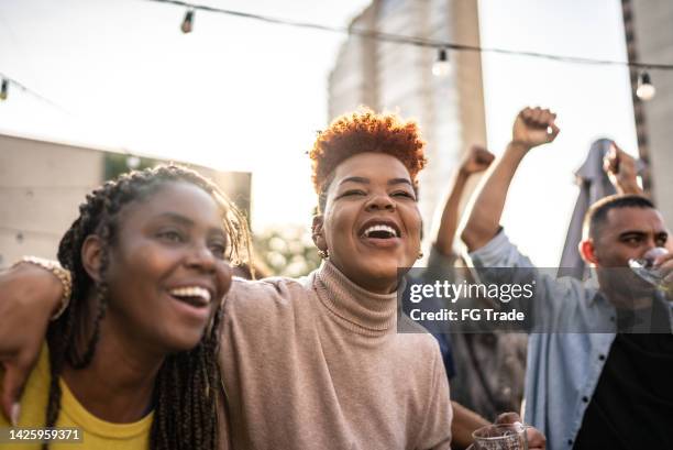 sports fans watching a match and celebrating at a bar rooftop - concert crowd stock pictures, royalty-free photos & images