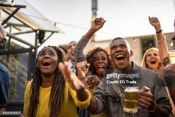 aficionados al deporte viendo un partido y celebrando en la azotea de un bar - reality tv fotografías e imágenes de stock