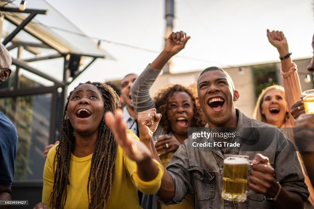 Sports fans watching a match and celebrating at a bar rooftop