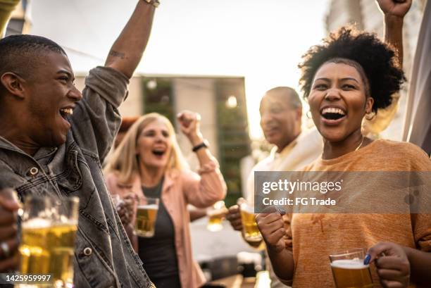 sports fans watching a match and celebrating at a bar rooftop - social tv awards stockfoto's en -beelden