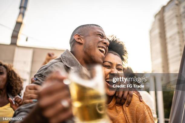 sports fans watching a match and celebrating at a bar rooftop - social tv awards stockfoto's en -beelden