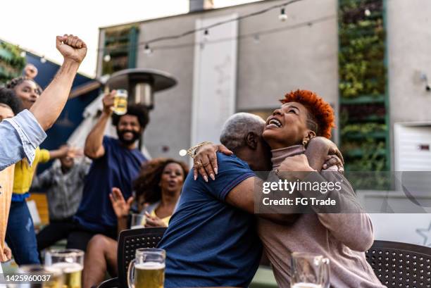 sports fans watching a match and celebrating at a bar rooftop - basketball match on tv stockfoto's en -beelden