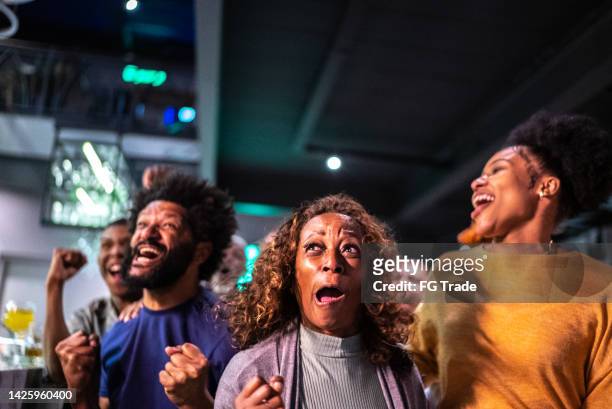 sports fans watching a match and celebrating at a bar - basketball fans stock pictures, royalty-free photos & images