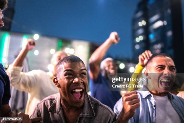 sports fans watching a match and celebrating at a bar rooftop - social tv awards stockfoto's en -beelden