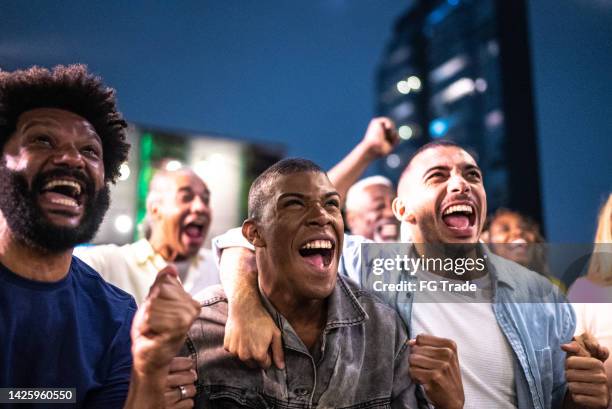 sports fans watching a match and celebrating at a bar rooftop - match sport stockfoto's en -beelden
