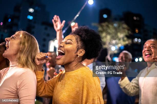 sports fans watching a match and celebrating at a bar rooftop - festival bar stockfoto's en -beelden