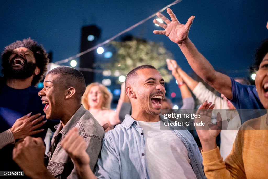Sports fans watching a match and celebrating at a bar rooftop