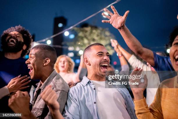 sports fans watching a match and celebrating at a bar rooftop - basketball fans stock pictures, royalty-free photos & images