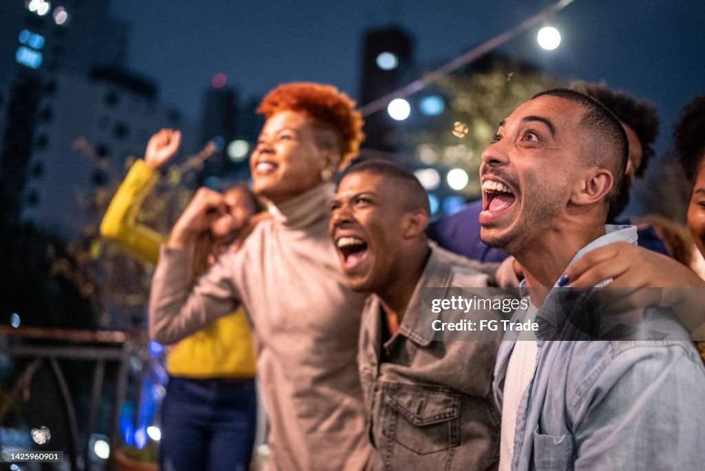 Sports fans watching a match and celebrating at a bar rooftop