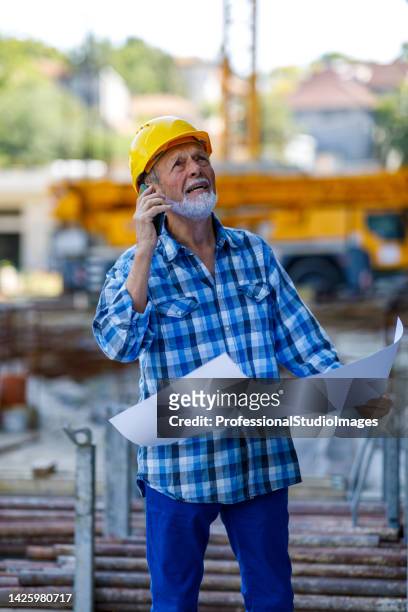 engenheiro sênior de construção está segurando um plano de papel e conversando com colegas de trabalho usando um telefone. - workers compensation - fotografias e filmes do acervo