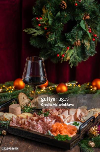 assiette d’apéritif de planche de charcuterie de noël avec salami, jambon, saumon et vin rouge pour noël dans une cuisine rustique sombre - verre vin rouge photos et images de collection