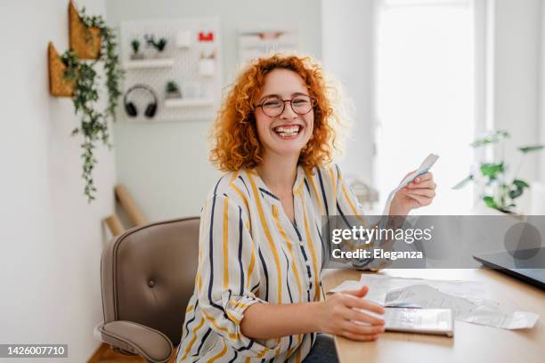 young redhead woman checking her home finances - bonnetje stockfoto's en -beelden