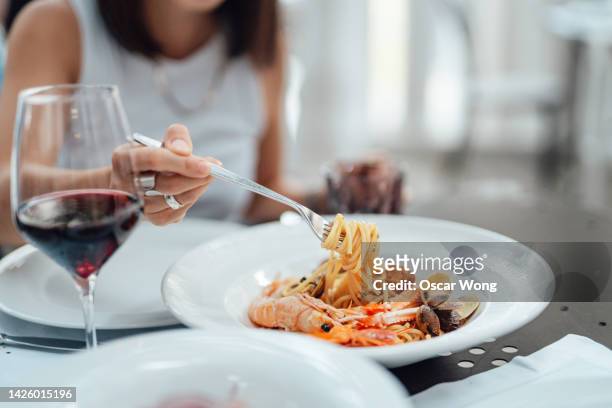 close-up of young woman eating fresh seafood pasta in restaurant - gourmet foto e immagini stock