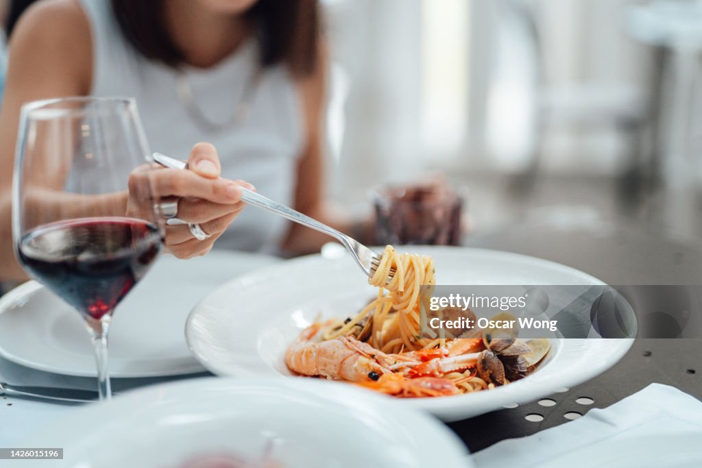 Close-up of young woman eating fresh seafood pasta in restaurant