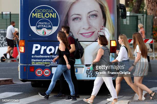 People walk a by an election poster showing Giorgia Meloni, leader of the 'Partito Fratelli D'Italia' , with the slogan "Ready to raise Italy", is...