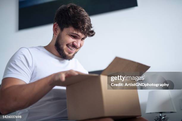 man at home opening a package he got in the mail. - opening a box stockfoto's en -beelden